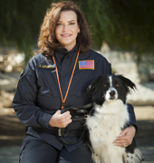 A woman in uniform poses, kneeling, next to a black-and-white border collie mix dog
